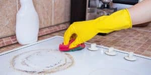 Hands Cleaning Stove Knobs With Yellow Gloves And Sponge